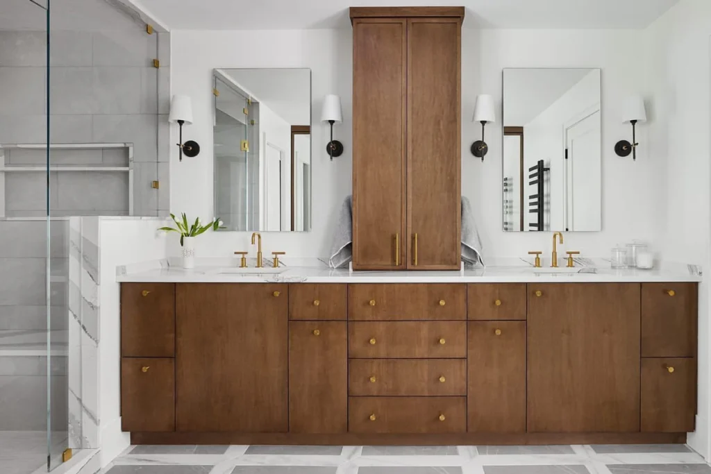 A jack and jill bathroom with wooden cabinets and mirror on the wall and gold fixture 