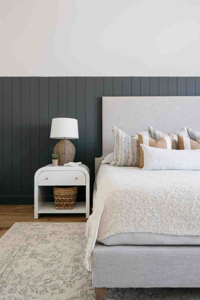 A dark grey beadboard with white nightstand and wooden floor on the rug 
