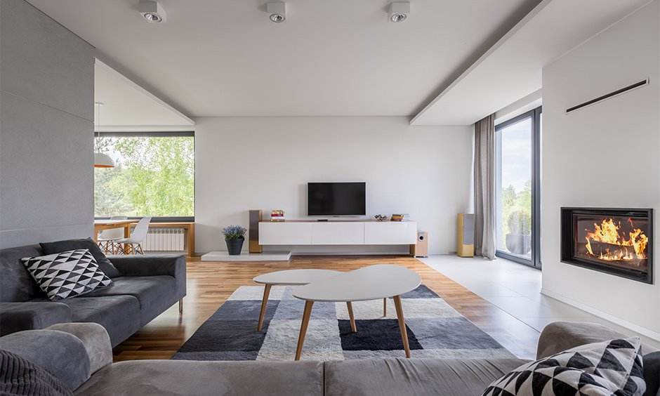 A white and grey living room with grey sofa and cushion on it and tv on the white wall