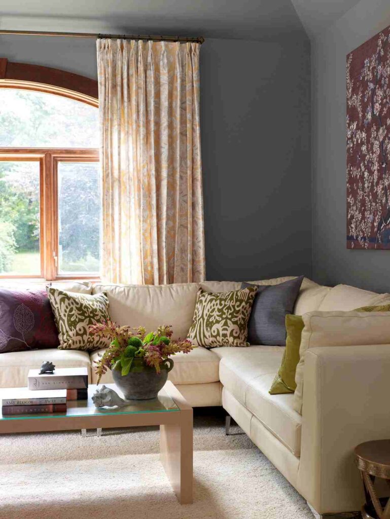 A grey living room with beige sofa and cushion and windows 