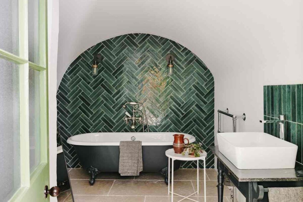 A grey bathroom with green tiles and grey bathtub and wooden floor and white sink