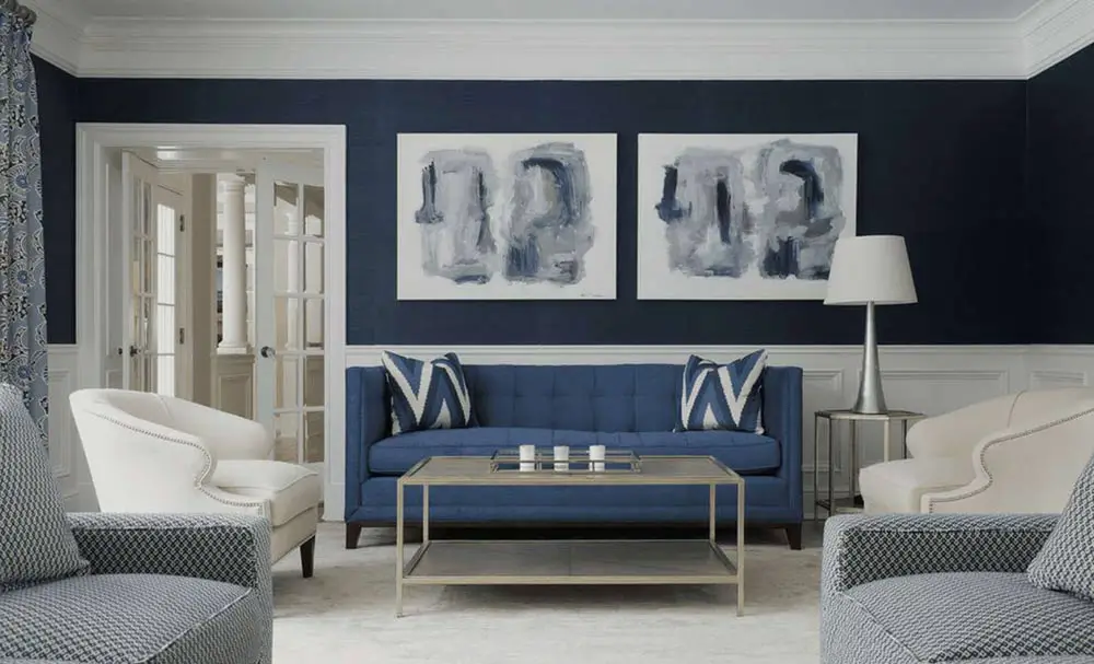 A navy and grey living room with grey lamp on side table and frames on the wll 