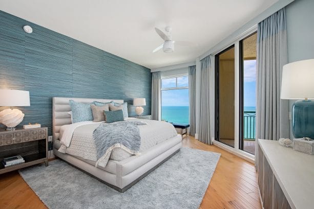 A teal wall in grey bedroom with grey bed and blanket on the bed and wooden floor with rug 