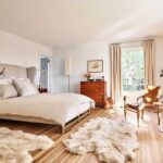 a-large-bed-with-tall-grey-headboard-light-wood-flooring-covered-by-a-large-white-fluffy-area-rug
