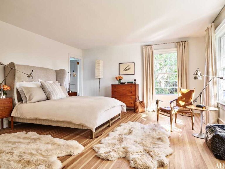 a-large-bed-with-tall-grey-headboard-light-wood-flooring-covered-by-a-large-white-fluffy-area-rug