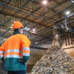 a-person-is-standing-infront-of-waste-moved-by-industrial-machinery