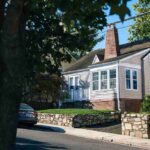 one-and-half-story-house-with-light-colored-siding-and-a-dark-roof-with-numerous-windows-across-the-front-and-back-chinmey