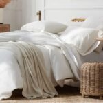 white-color-bed-with-white-linen-quilt-cover-pillows-bedsheet-and-brown-small-stool-near-bed