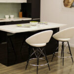 white-kitchen-island-with-a-sleek-black-base-is-placed-at-the-center-and-two-white-bar-stools-with-metal-legs-are-neatly-arranged-beside-the-island