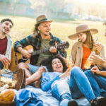 a-group-of-young-friends-enjoying-a-picnic-together-in-a-park-they-are-sitting-on-a-blanket-on-the-grass-in-an-open-outdoor-area