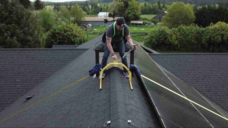 a-person-wearing-a-safety-harness-is-positioned-on-the-peak-of-an-asphalt-shingle-roof