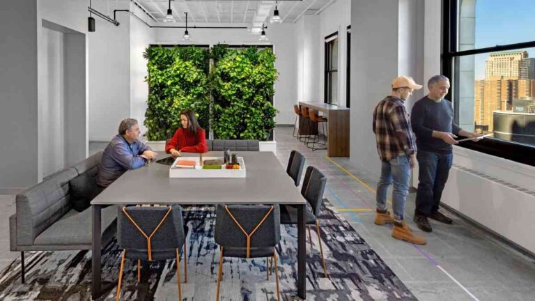 5 Ways Office Design Affects Focus and Employee Wellbeing modern-office-interior-the-space-is-bright-with-white-walls-in-middle-there-is-a-large-rectangular-table-two-people-were-standing-and-two-were-sitting
