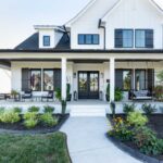 the-house-has-a-light-colored-exterior-with-a-dark-roof-the-entrance-has-double-doors-with-glass-panels-and-windows-with-dark-shutters
