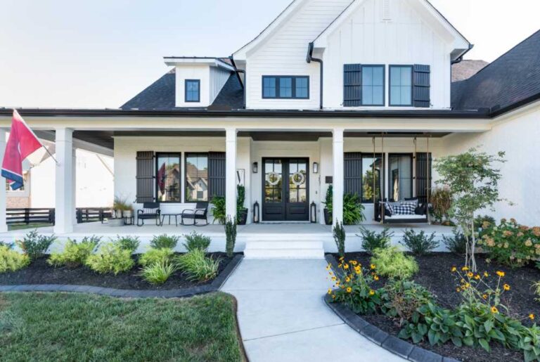 the-house-has-a-light-colored-exterior-with-a-dark-roof-the-entrance-has-double-doors-with-glass-panels-and-windows-with-dark-shutters