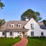 he-house-is-painted-white-with-a-cedar-exterior-on-both-the-walls-and-roof-and-multiple-white-framed-windows-and-house-is-surrounded-by-well-maintained-green-lawn-trees-shurbs