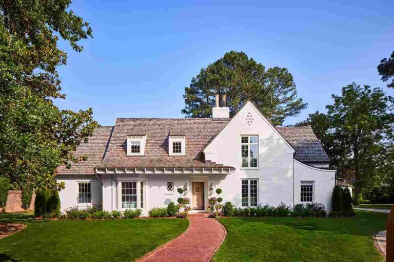 he-house-is-painted-white-with-a-cedar-exterior-on-both-the-walls-and-roof-and-multiple-white-framed-windows-and-house-is-surrounded-by-well-maintained-green-lawn-trees-shurbs