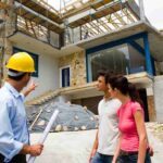 three-people-are-standing-and-looking-towards-the-building-a-man-wearing-a-yellow-hat-pointing-towards-construction-and-house-is-built-featuring-a-large-glass-windows
