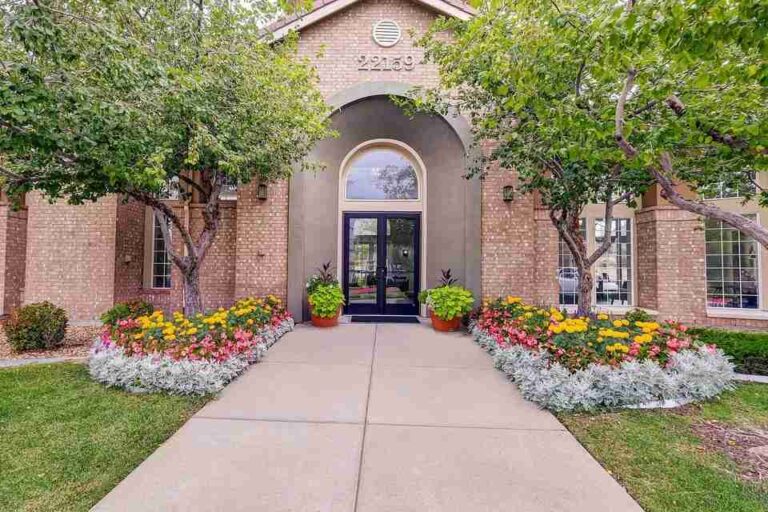 traditional-architectural-style-with-a-light-colored-brick-and-large-arched-entryway-and-entrance-is-framed-by-dark-glass-double-door-a-paved-walkway-well-maintained-lawn