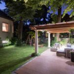 a-raised-patio-made-of-composite-decking-leads-to-a-white-wooden-pergola-structure-and-outdoor-furniture-including-couch-chair