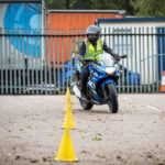 person-wearing-a-helmet-and-high-visibility-vest-actively-riding-a-motorcycyle-in-a-paved-fenced-area