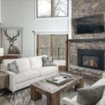 spacious-living-room-featuring-a-fireplace-and-a-spiral-staircaise-the-rooms-focal-point-is-a-stone-fireplace-and-white-sectional-sofa-with-seperate-armchair