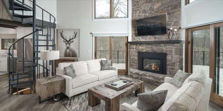 spacious-living-room-featuring-a-fireplace-and-a-spiral-staircaise-the-rooms-focal-point-is-a-stone-fireplace-and-white-sectional-sofa-with-seperate-armchair