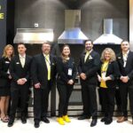 team-of-professionals-likely-representatives-from-thor-kitchen-standing-in-front-of-a-row-of-stainless-steel-kitchen