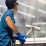 the-man-is-wearing-gloves-while-cleaning-the-glass-with-long-handled-squeegee