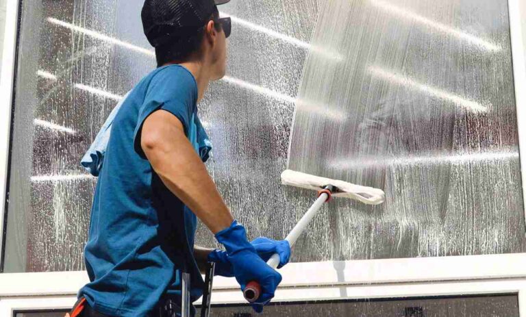 Why We Recommend Window Cleaning After Pressure Washing Service the-man-is-wearing-gloves-while-cleaning-the-glass-with-long-handled-squeegee