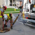 two-utility-workers-performing-maintenance-or-inspection-work-on-a-manhole-in-a-residential-street
