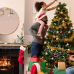 warm-festive-scene-of-a-family-decorating-for-the-holidays-in-their-living-room-a-man-is-holding-a-young-girl-so-she-can-reach-the-top-of-the-tree