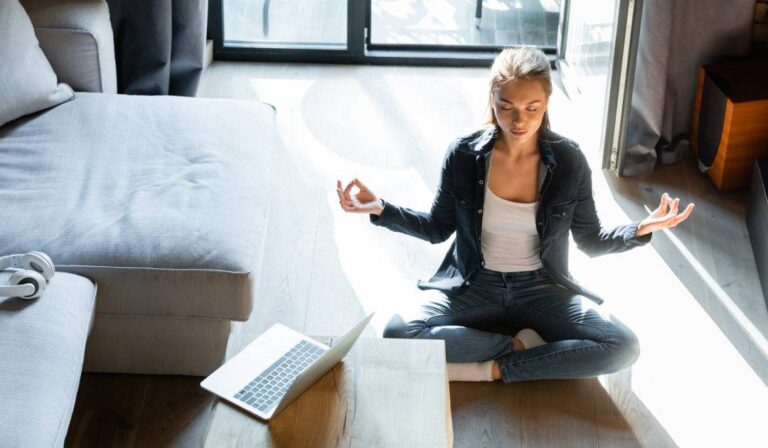 Small Habits, Big Impact: How to Build a Feel-Good Lifestyle at Home a-women-is-seated-in-a-cross-legged-lotus-position-on-a-light-colored-rug-she-is-practicing-a-yoga