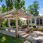 open-concept-outdoor-living-space-featuring-a-large-white-pergola-situated-on-a-stone-paver-patio