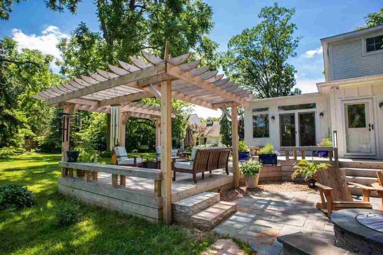 Pergolas, Shade Sails, and Other Deck Add-Ons Worth the Investment open-concept-outdoor-living-space-featuring-a-large-white-pergola-situated-on-a-stone-paver-patio