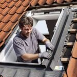 roofing-professional-installing-a-roof-window-into-a-sloped-roof-with-red-tiles