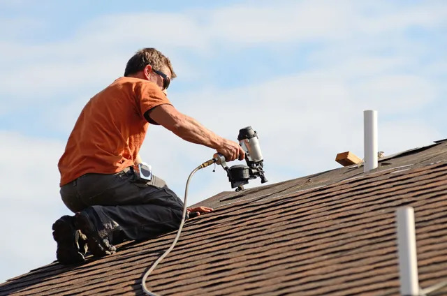 How to Choose the Right Roofing Contractor: 5 Red Flags to Watch Out For the-roofer-is-kneeling-on-the-shingles-and-using-a-pneumatic-nail-gun-to-secure-the-roofing-material