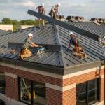 workers-are-shown-on-a-dark-grey-or-black-metal-roof-using-tools-and-ladders-to-secure-long-naarrow-metal-panel