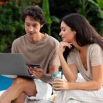 a-girl-and-boy-sitting-near-a-pool-boy-is-using-laptop-and-girl-watching-the-screen