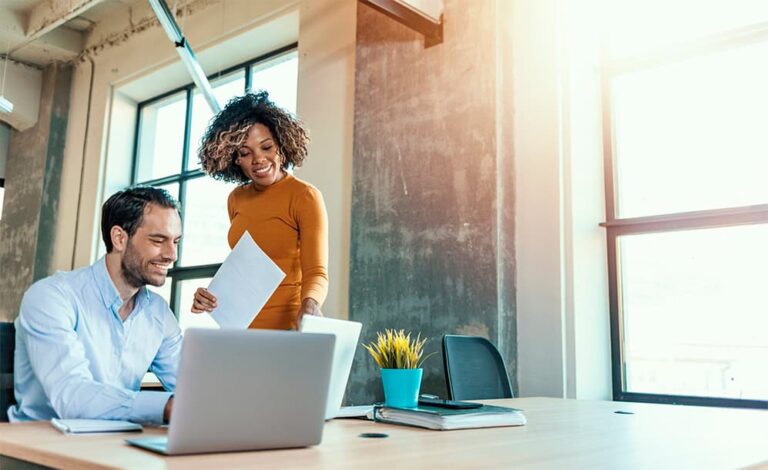 Exiting Help to Buy: Your Complete Guide to Loan Redemption a-man-and-a-woman-in-an-office-and-man-man-doing-work-in-laptop-while-smiling-and-girl-holding-a-paper-and-seeing-a-laptop