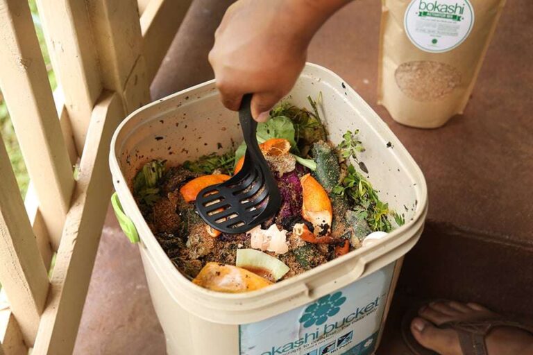 a-person-mixing-food-waste-and-organic-scraps-inside-a-compost-container-using-a-black-scoop