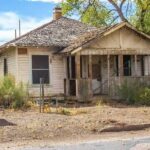 a-single-story-home-features-damaged-front-porch-with-peeling-white-paint-and-a-weathered-wood-shake-roof
