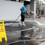 a-worker-using-a-commercial-pressure-washer-to-clean-a-large-outdoor-surface-likely-a-parking-lot-walkway-or-industrial-courtyard