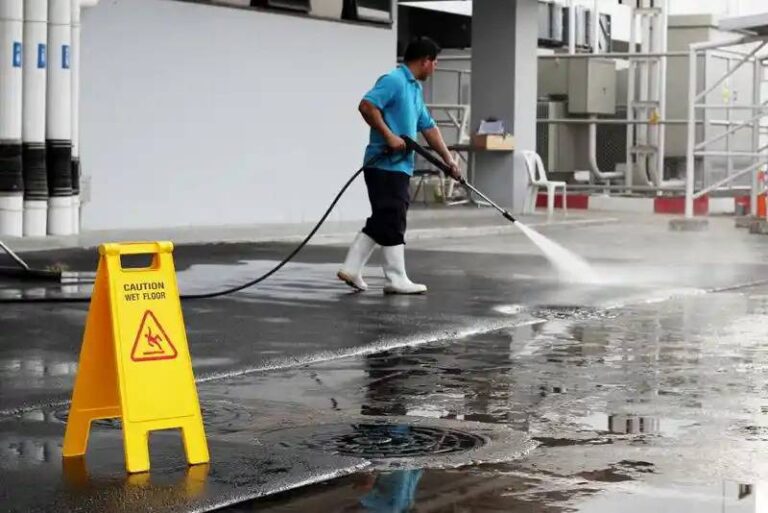 a-worker-using-a-commercial-pressure-washer-to-clean-a-large-outdoor-surface-likely-a-parking-lot-walkway-or-industrial-courtyard