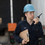a-worker-wearing-a-blue-safety-helmet-and-communicating-through-a-two-way-radio-he-is-holding-documents