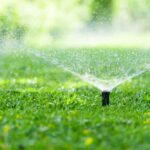 an-outdoor-scene-featuring-an-active-pop-up-lawn-sprinkler-system-watering-a-vibrant-green-grass-lawn