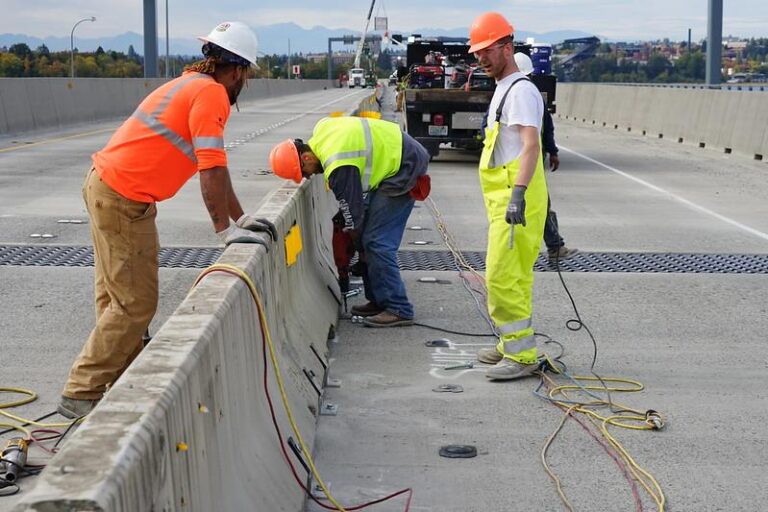 three-construction-workers-wearing-safety-gear-on-a-road-construction-site-and-installing-aligning-or-security-heavy-concrete-barriers-on-a-roadway