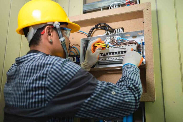 What to Do in an Electrical Emergency at Home a-electrician-using-a-screwdriver-to-adjust-or-install-wiring-inside-an-open-electrical-breaker-box-mounted-on-a-wall