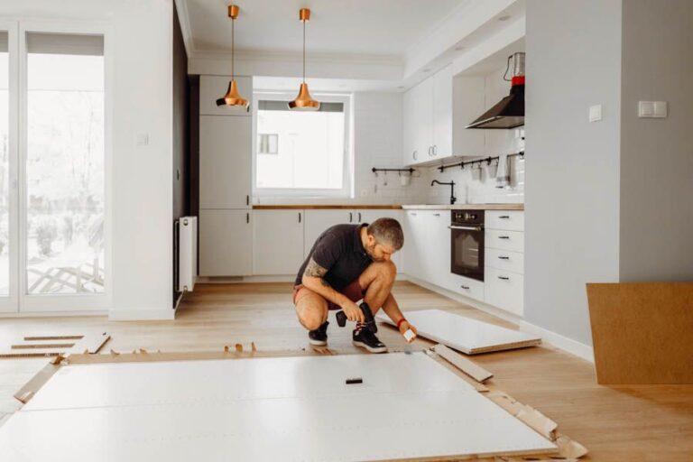 a-man-is-crouching-down-on-the-floor-he-appears-focused-and-is-working-with-his-hands-to-measure-or-lay-down-pieces-of-wood