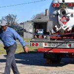 a-man-is-walking-outdoor-across-an-asphalt-driveway-or-road-next-to-a-large-service-truck