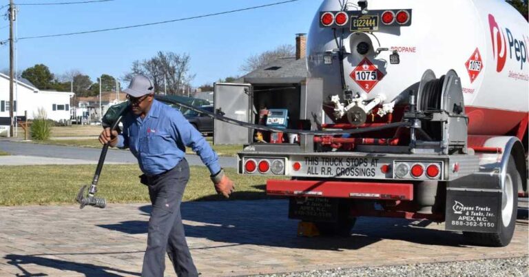 a-man-is-walking-outdoor-across-an-asphalt-driveway-or-road-next-to-a-large-service-truck